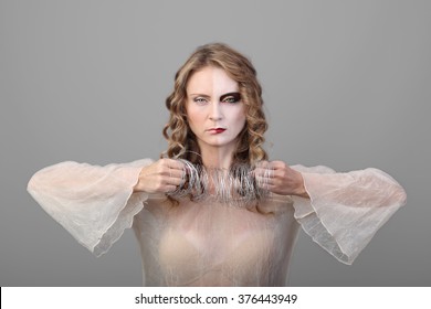 Pretty Young Woman With Long Wavy Hair And Pale Angry Makeup On Half Of Face Stands With Skein Of Wire In Hands On Gray Background - Unwanted Relations Concept
	