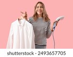 Pretty young woman with modern garment steamer and shirt on pink background