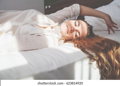 Pretty young woman on bed in modern apartment smiling after wake up