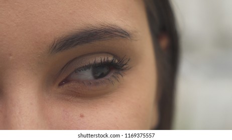 Pretty young woman opening her eye. Macro close up of female eyelid lifting. Brunette girl looking to the side and smiling