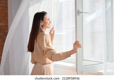 Pretty young woman opening window in room - Shutterstock ID 2128958936