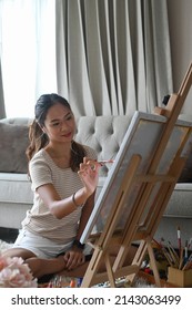 Pretty Young Woman Painting A Picture On Canvas In Bright Living Room.