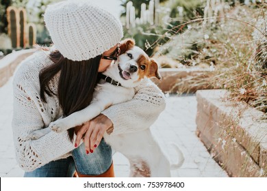 Pretty young woman playing with her adorable dog Jack Rusell in a park surrounded by cactus and a small pond. Adorable sunny autumn day. Lifestyle.