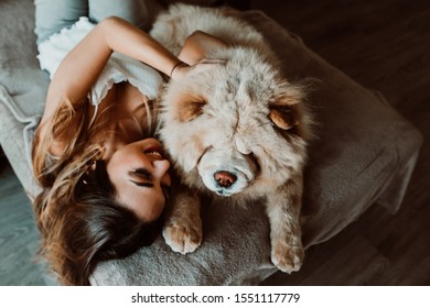 
Pretty Young Woman Playing And Sharing Her Time At Home With Her Chow Chow Dog. Lying On The Couch Relaxed And Carefree. Lifestyle