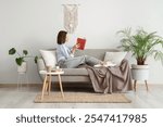 Pretty young woman reading book on sofa near white wall