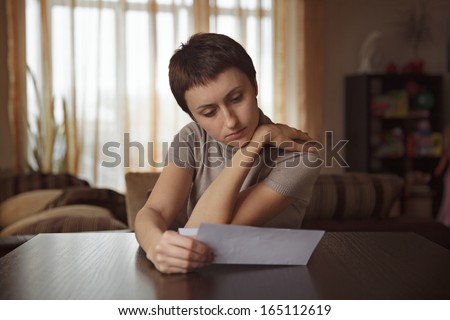 Pretty young woman reading a letter at the table