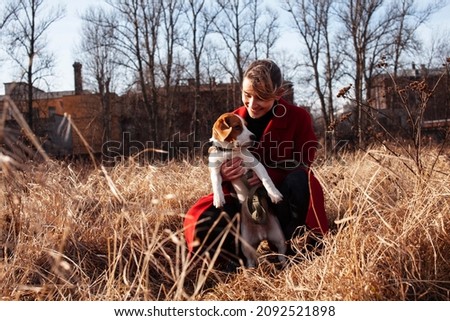 pretty young woman in red coat playing with dog outside in park, lifestyle people concept