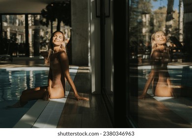 Pretty young woman relaxing by the indoor swimming pool - Shutterstock ID 2380346963