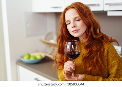 Pretty Young Woman Relaxing With A Glass Of Red Wine Standing With Her Eyes Closed In Bliss Leaning Against A Kitchen Counter At Home