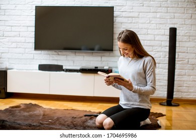 Pretty young woman relaxing on floor at home while reading a book - Shutterstock ID 1704695986