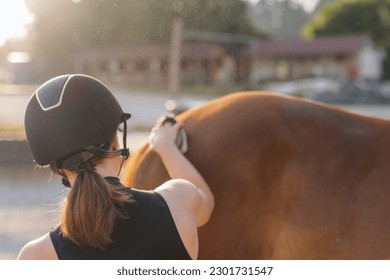 Pretty young woman with a riding helmet brushing her beautiful red horse before ride in nature. Grooming time concept. - Powered by Shutterstock