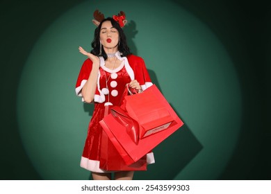 Pretty young woman in Santa costume with shopping bags blowing kiss on green background - Powered by Shutterstock