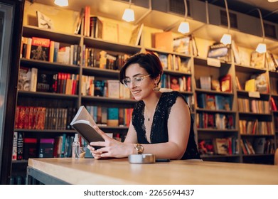 A pretty young woman with shirt hair wearing casual outfit reading a book in a cozy cafe. Young woman is spending her free time at bookstore and reading a book. - Powered by Shutterstock