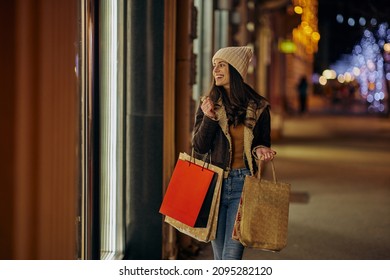 Pretty young woman with shopping bags by the shop window at Christmas time