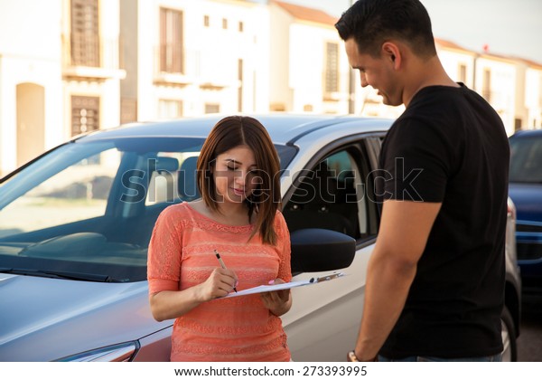 Pretty young woman signing a new car lease\
with a salesperson
