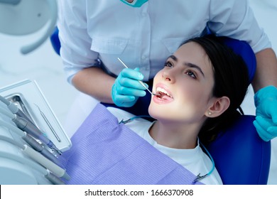 Pretty young woman sitting in dental chair at medical center while professional doctor fixing her teeth. Healthy teeth