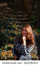 Pretty Young Woman Is Sitting On The Stairs At Sunset In Beautiful Autumn Forest. Colorful Autumn Landscape With Alone Girl In Dress And Fall Leaves. Travel And Adventure In Europe. Grza, Serbia.