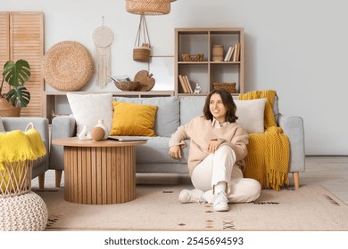 Pretty young woman sitting on floor near grey sofa in light living room - Powered by Shutterstock