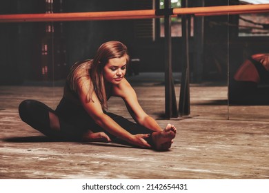 Pretty young woman slavic in sports uniform works out in evening in an old gym, doing stretching exercises in front of mirror. Concept of healthy lifestyle, sport and exercise in gym. Copy space