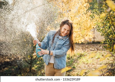 Pretty young woman splashing champagne on the nature at sunset