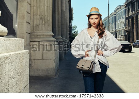 Pretty young woman stands on a city street on a sunny summer day. Summer vacation, trips. Fashion.