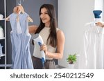 Pretty young woman steaming clothes with modern garment steamer in laundry room