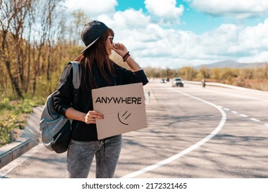 Pretty young woman in sunglasses and cap holding a cardboard sign with text anywhere. The concept of local traveling and hitchhiking.
