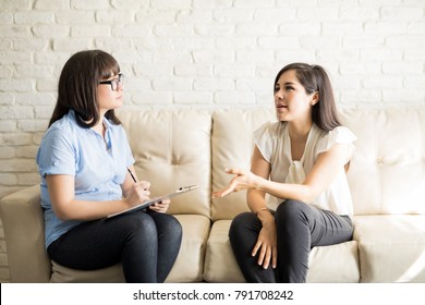 Pretty Young Woman Talking To Female Therapist On Sofa, Sharing Her Issues During Psychotherapy.