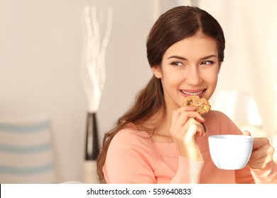 Pretty young woman with tasty cookie and cup of tea at home