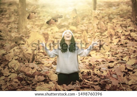 Pretty young woman throwing autumn leaves while enjoying holiday. Shot outdoors