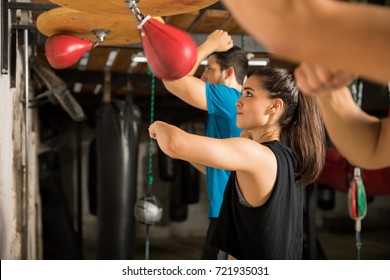 Pretty young woman training with a speed bag with a group of people in a boxing gym - Powered by Shutterstock