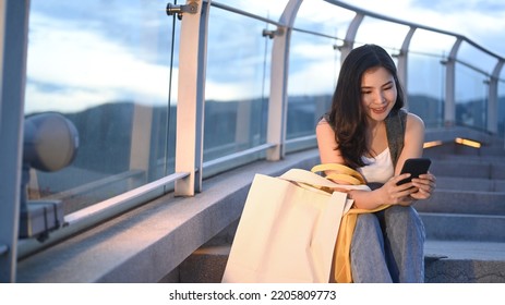 Pretty Young Woman Using Mobile Phone And Sitting On Stairs With Beautiful Evening Sky In Background