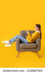 Pretty young woman using tablet computer in soft armchair on yellow background - Shutterstock ID 2128407503