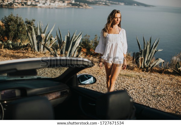 Pretty\
young woman walking to cabriolet car at\
seaside