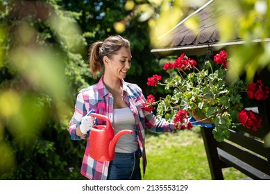 Pretty young woman  watering flowers in garden in summer time - Powered by Shutterstock