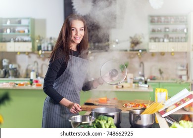 Pretty Young Woman Wearing Apron Making Dinner Cooking Spaghetti Following The Recipe In A Book Standing In Kitchen