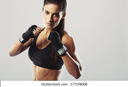 Pretty young woman wearing boxing gloves posing in combat stance looking at camera. Fit young female boxer ready for fight on grey background - Powered by Shutterstock