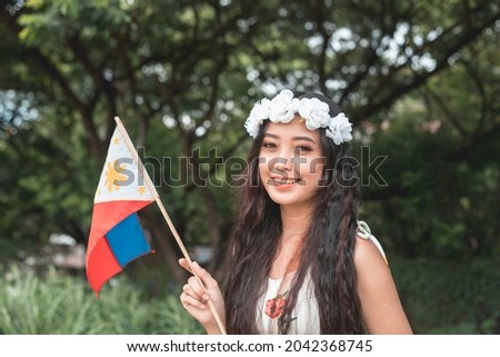 A pretty young woman wearing a floral headband holds a Philippine Flag.