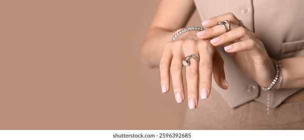 Mujer joven bonita que lleva la joyería elegante de la plata en el fondo beige con el espacio para el texto, primer plano