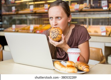Pretty young woman working at the computer and eat bread. Unhealthy Lifestyle