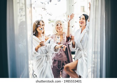 Pretty young women friends in bathrobes and pajama clink elegant glasses with delicious champagne at bachelorette party on hotel room terrace