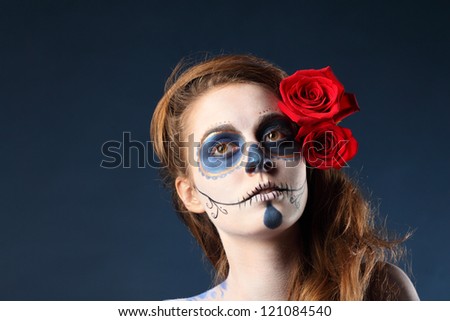 Pretty zombie girl with painted face and two red roses in her hair looks away.