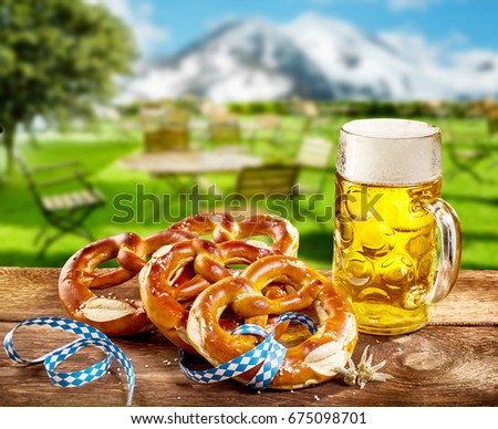 Pretzels and frothy pint of beer in a glass tankard to celebrate Oktoberfest served on a rustic wooden table outdoors in a tavern with a view of the snowy alps