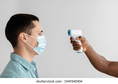 Prevent Covid-19 Virus, First Symptoms And Preparation For Vaccination. African American Doctor Taking Temperature With Infrared Thermometer At Young Patient In Clinic, Free Space, Close Up, Profile