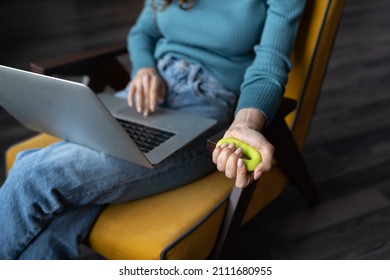 Preventing carpal tunnel syndrome. Cropped photo of woman working on laptop doing daily exercises with expander or hand grip ring to help improve overall grip strength in your hand, selective focus