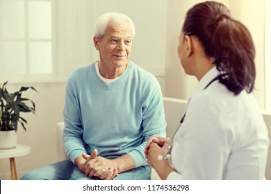 Preventive consultation. Selective focus on a cheerful senior gentleman sitting on a sofa and listening to a female medical worker during a checkup. - Shutterstock ID 1174536298