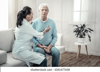 Preventive examination. Old pleasant embarrassing man sitting in the white room near the nurse having medical examination and looking straight. - Shutterstock ID 1041477658