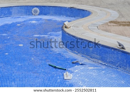 Preventive maintenance of the swimming pool before the start of the summer season, grouting the seams of the blue mosaic coating of the walls and bottom of the pool with simple tools