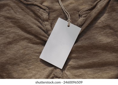 Price tag with rope hanging on folded beige cotton t-shirt. Closeup of blank label mockup of clothing item. Clothes, fashion and shopping concept. Branding display, top view. No people. - Powered by Shutterstock