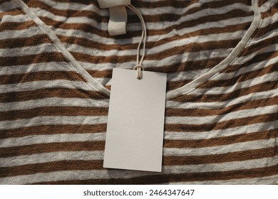 Price tag with rope hanging on folded beige linen white and rusty brown striped t-shirt. Closeup of blank label mockup of clothing item. Clothes, fashion. Shopping concept. Branding display. Top view - Powered by Shutterstock